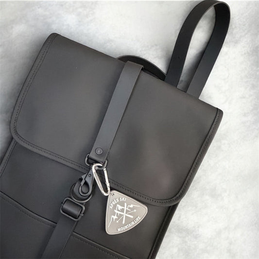 Minimalist ski accessory styling. Grey Après Ski charm attached to a black backpack strap. Aesthetic bag charm for winter travel and mountain trips.