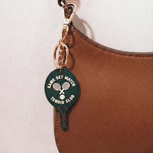 Tennis racket charm attached to a brown leather bag.