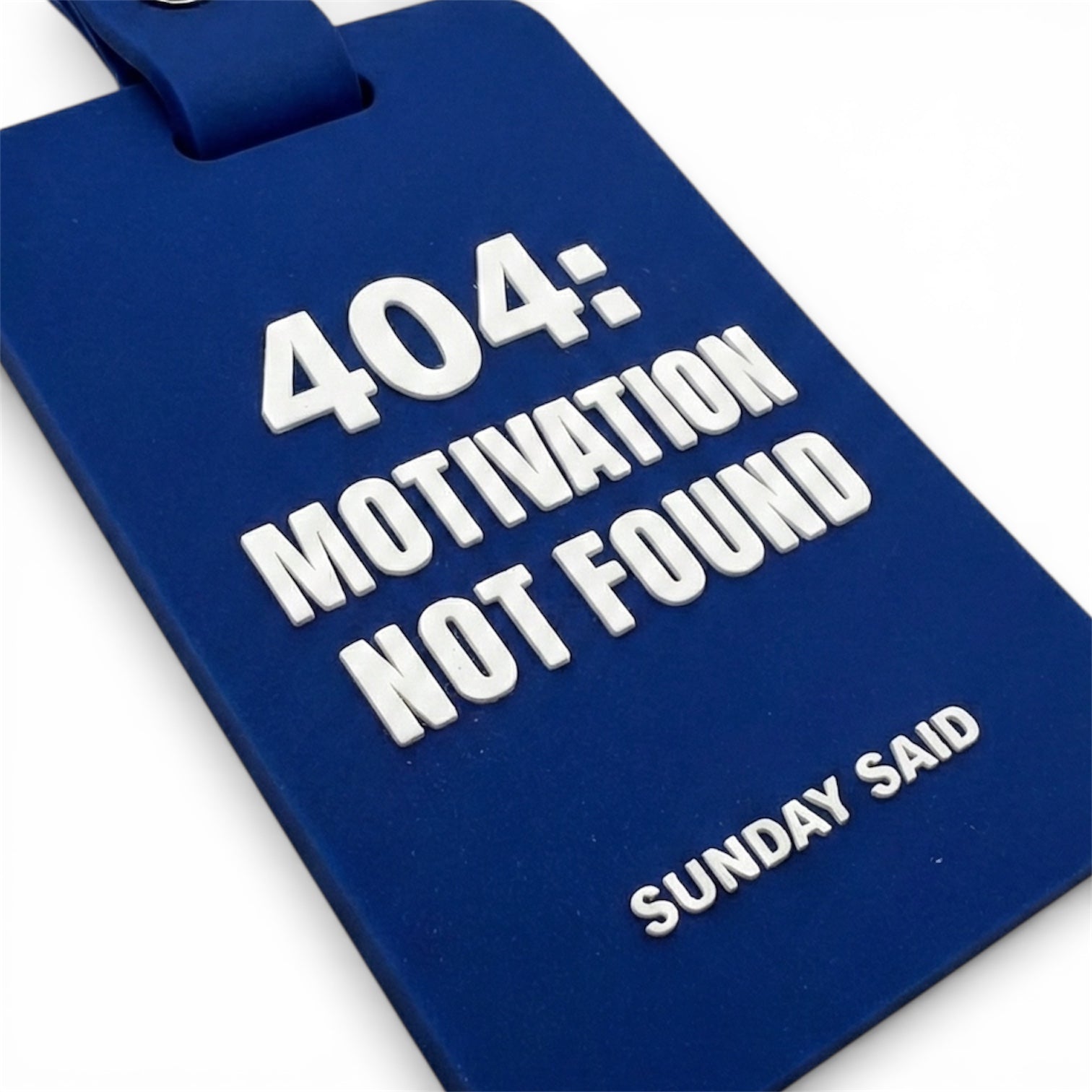Close up of high quality 3D raised white lettering on blue rubber tag. Detail showing 404 Motivation Not Found quote. Durable silicone bag accessory.