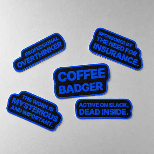 Five black and blue Sunday Said workplace stickers on a silver-gray background with phrases about Slack, coffee, overthinking, insurance, and mysterious work.
