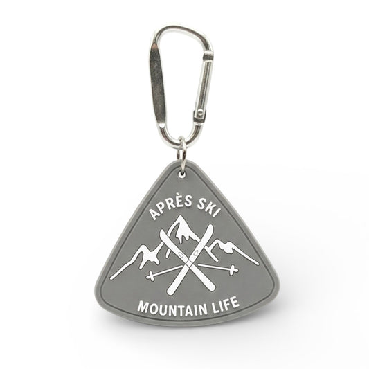 Sunday Said Après Ski bag charm. Grey triangular rubber keychain featuring crossed skis and Mountain Life text. Perfect winter sport gift for skiers.