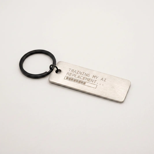 Metal keychain with text 'Training my AI replacement...' on a light gray background